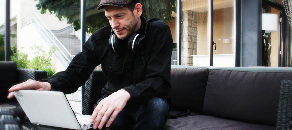 Selbstportrait DJ Jürgen Haslauer. Ich sitze auf einer Bank und blicke in meinen geöffneten Laptop.